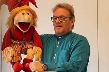 Bauredner Patrick Martin mit einer Puppe im Harlekin-Kostüm
