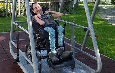 Ein junger Rollstuhlfahrer sitzt auf einer Schaukel, die extra für Rollstühle konzipiert wurde.