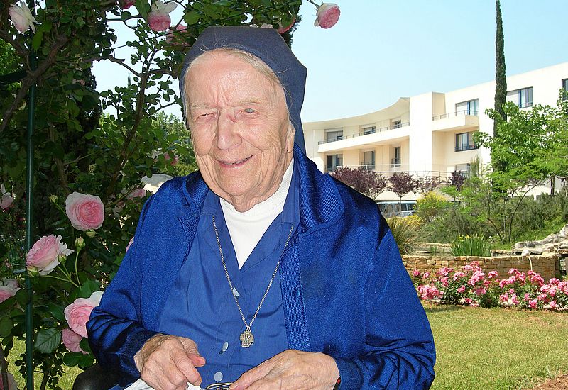 Schwester André Randon steht in einem Garten und lächelt in die Kamera. 