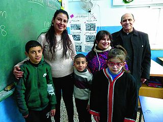 Schülerinnen und Schüler mit ihrer Lehrerin Marina und Pater Mamdouh in einem Klassenzimmer. 