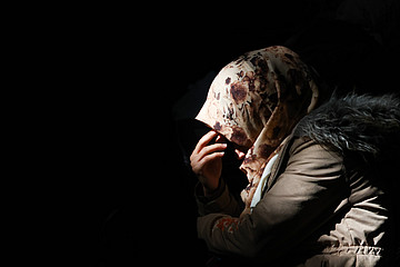 Frau mit Kopftuch hält Hand vors Gesicht