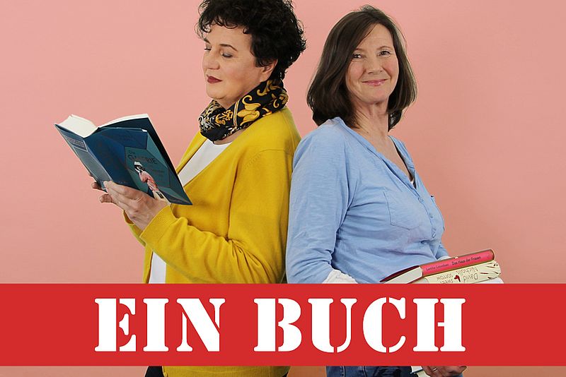 Susanne Steufmehl und Gabie Hafner stehen Rücken an Rücken. Steufmehl liest ein Buch, Hafner hält einen Bücherstapel fest.