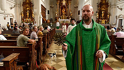 Stephan Zinner in seiner Rolle als Pfarrer Hans Reiser, mit grünem Gewand in einer mit Menschen besetzten Kirche.