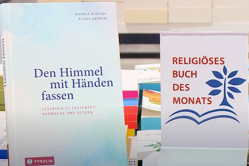Das Buch "Den Himmel mit Händen fassen" neben einem Aufsteller mit der Bezeichnung "Religiöses Buch des Monats"