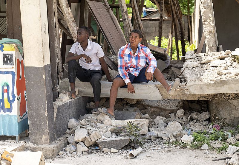 Zwei Menschen sitzen in der Ruine eines durch das Erdbeben zertörten Hauses in Haiti.