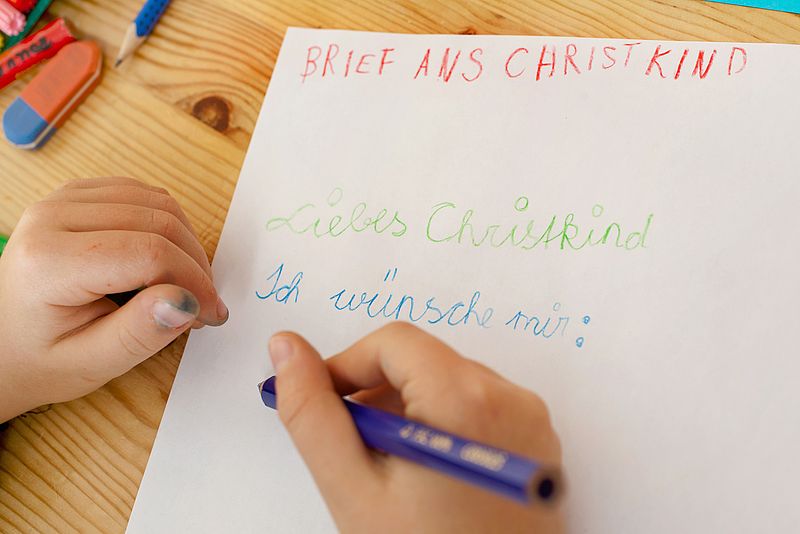 Hand zu sehen, die mit einem bunten Stift einen Brief schreibt. "Liebes Christkind" ist auf dem Papier zu lesen. 