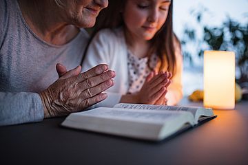 Kind betet mit älterer Frau vor aufgeschlagener Bibel