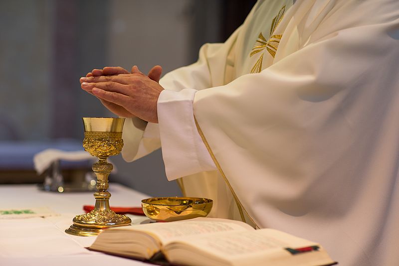 Hände des Priesters beim Hochgebet, Kelch und Schale stehen auf Altar