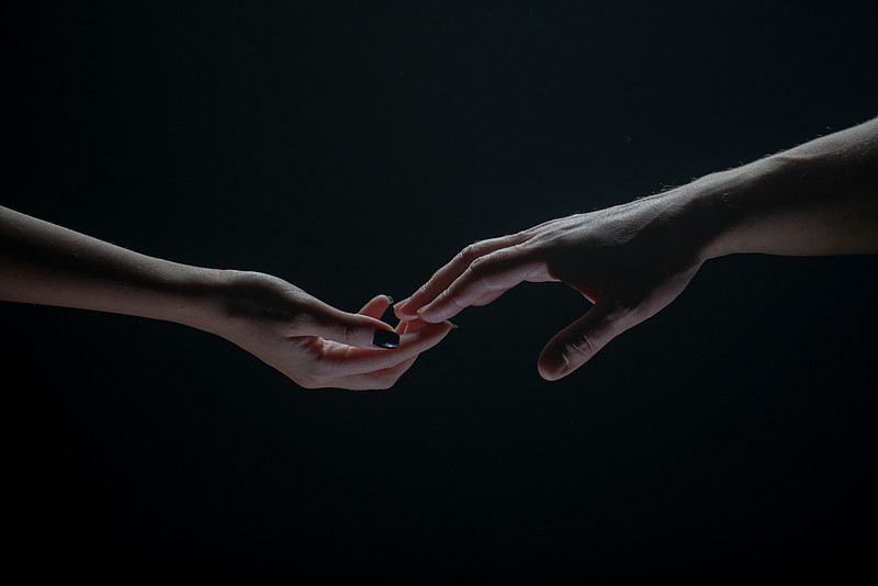 Zwei Hände greifen vor dunklem Hintergrund nacheinander