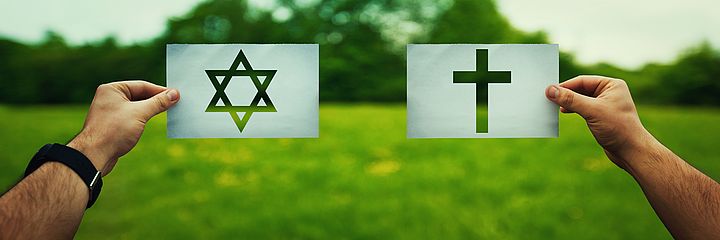 Kreuz und Davidstern werden auf Papier auf einer grünen Wiese gehalten.