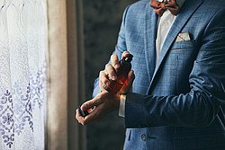 Ein Mann in Anzug besprüht sein Handgelenk mit Parfüm