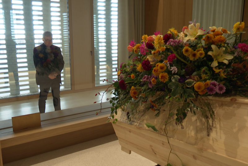Mann steht vor mit Blumen dekoriertem Sarg