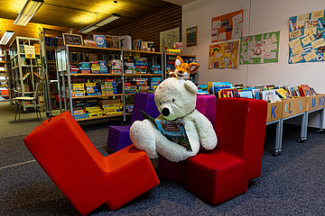 Hier sieht man die Echinger Gemeindebücherei von Innen. Auf roten Sesseln sitzt ein Teddybär.