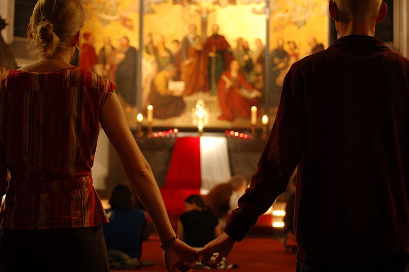 Zwei Menschen halten sich an den Händen, im Hintergrund ein Altar