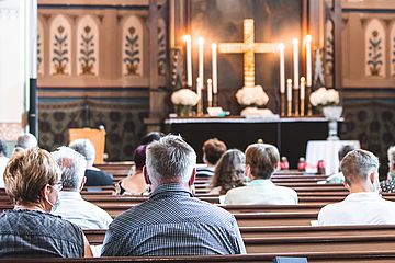 Menschen sitzen auf Kirchenbänken und nehmen an einem Gottesdienst teil. 