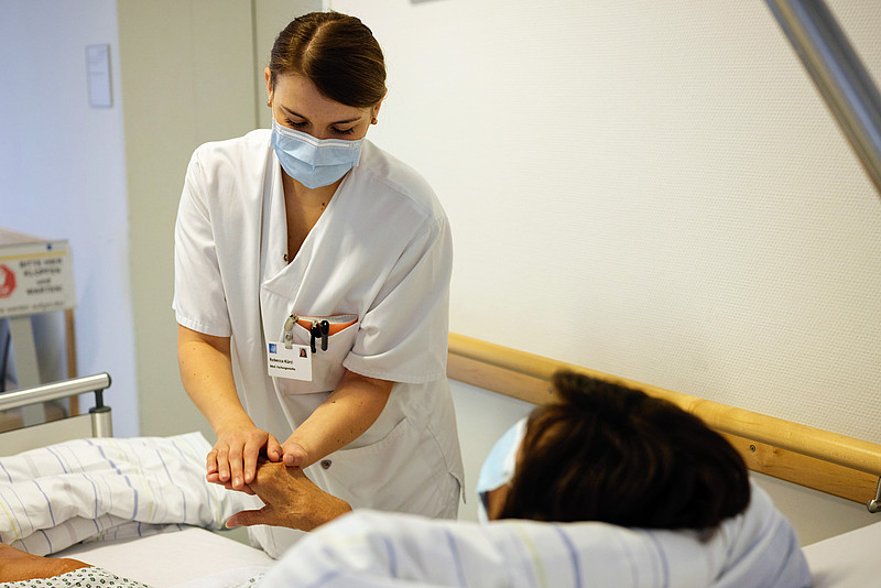 Eine medizinische Fachkraft hält die Hand einer Patientin, die in einem Bett auf dem Gang der Notaufnahme liegt, im Krankenhaus Barmherzige Brüder in Regensburg
