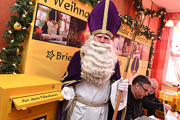 Mann in Nikolauskostüm steht vor Briefkasten mit der Aufschrift: An den Nikolaus.