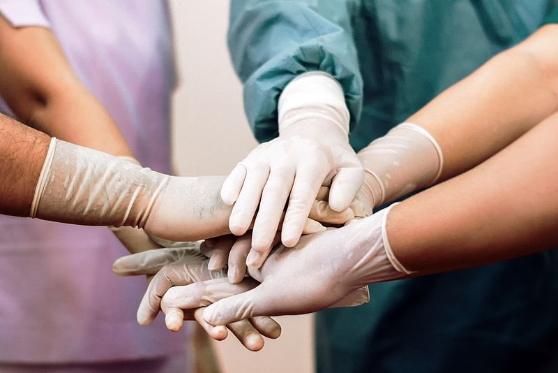 Menschen in OP-Kitteln halten Hände mit Handschuhen aufeinander