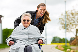 Junge Frau schiebt alte Frau im Rollstuhl