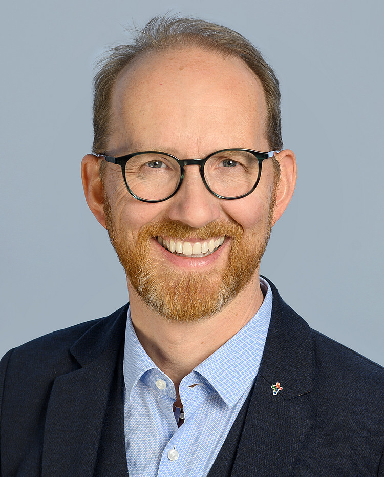 Porträt von Pfarrer Hofstetter, lächelnd im Anzug, mit Brille und Bart