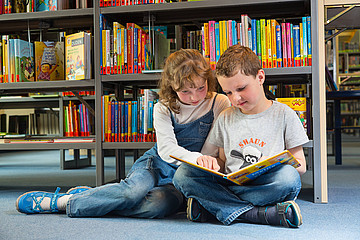 Ein Bub und ein Mädchen lesen gemeinsam ein Kinderbuch, der Bub deutet auf eine ihm wichtige Stelle.