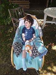 Die zehnjährige Hanne liegt lachend auf einem mit Decken ausgelegten Stuhl im Sommer im Garten.