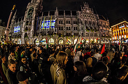 Münchner Marienplatz gefüllt mit vielen Menschen, die Palästina-Flaggen hochhalten, während das Rathaus mit der israelischen Flagge angestrahlt ist.