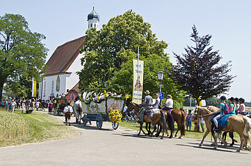 Pferde und Kutschen, Menschen in Tracht im Hintergrund eine Kirche