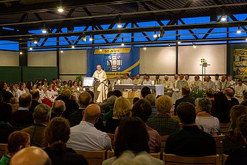 Weihbischof Haßlberger steht am Ambo und predigt. Menschen sitzen in Reihen und hören ihm zu. Von ihnen sind nur die Hinterköpfe zu sehen. 