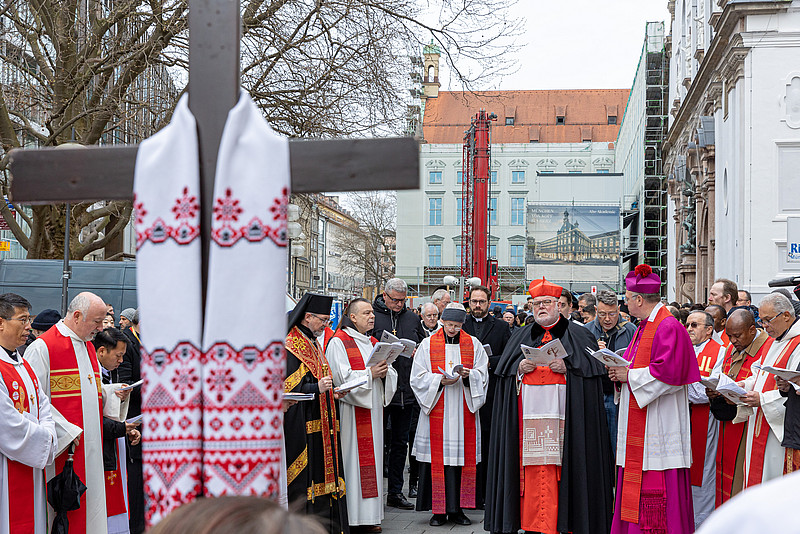 Kardinal Reinhard Marx mit Menschen vor einem Kreuz. 