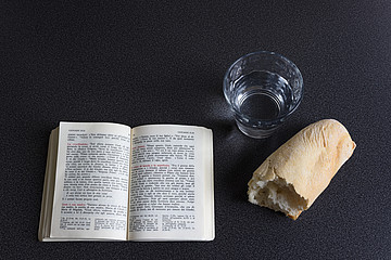 Aufgeschlagene Bibel neben Brot und Glas Wasser