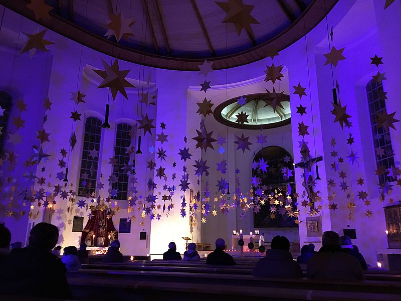 Menschen sitzen in blau beleuchteter Kirche über ihnen hängen Papiersterne