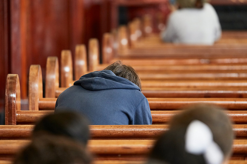 Fokus auf einem jungen Mann, der gnbaebeugt in Kirchenbank sitzt
