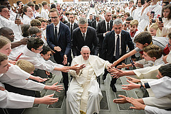 Ministranten aus Frankreich strecken die Hände aus, während Papst Franziskus im Rollstuhl an ihnen vorbeifährt.