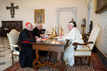 Kardinal Marx und Papst Franziskus sitzen mit einem weiteren Mann an einem Tisch