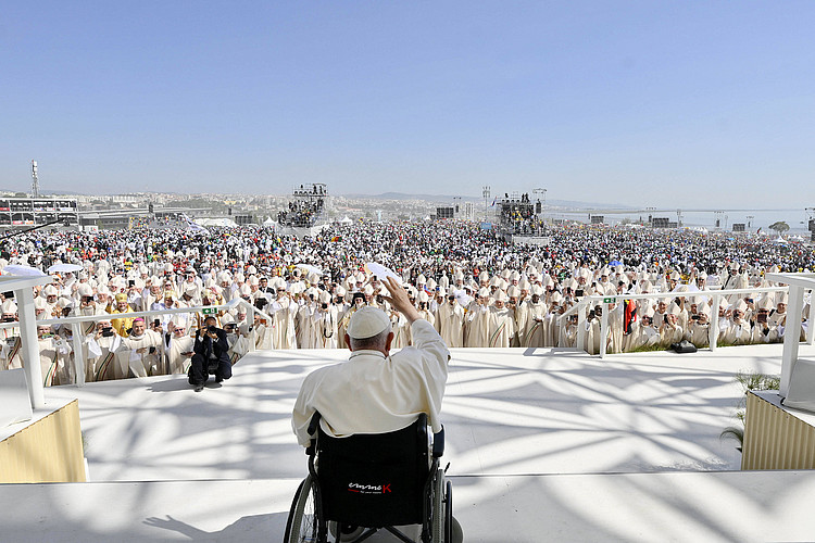 Papst Franziskus im Rollstuhl von hinten blickt von Bühne auf Menschenmenge