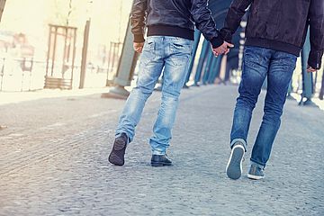 Zwei Männer gehen auf der Straße spazieren und halten Händchen. Ihre Gesichter sind nicht zu sehen.