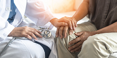 Ein Arzt hält mit der rechten Hand ein Stetoskop und mit der rechten die Hand eines Patienten