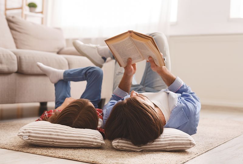 Erwachsener und Kind liegen auf dem Boden und lesen