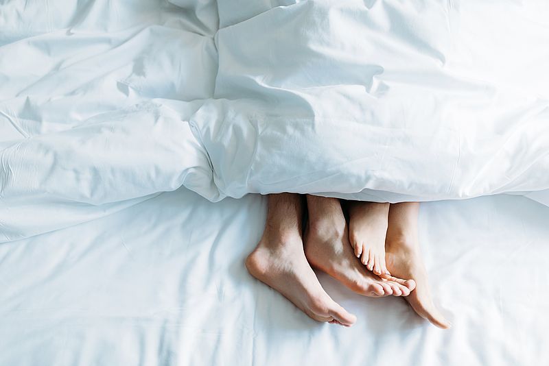 Zwei Paar Füße schauen unter einer Bettdeckee hervor