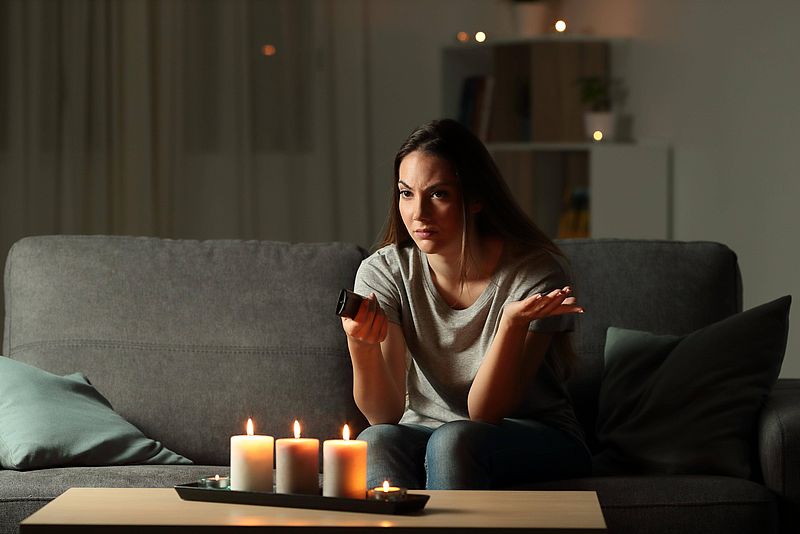 Frau mit Fernbedienung auf Sofa mit Kerzen