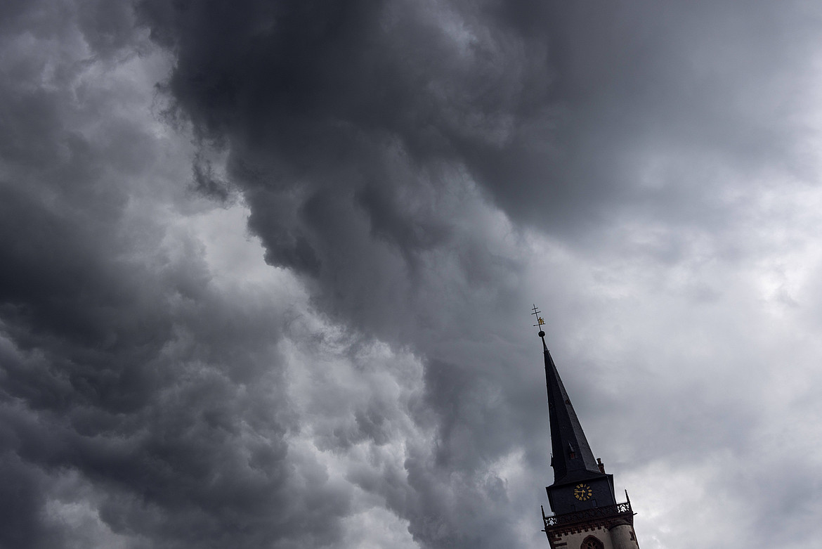 Dunkle Wolken eines Schauers sind am Abend am Himmel über dem Kirchturm der katholischen Kirche St.-Ursula in Oberursel zu sehen.