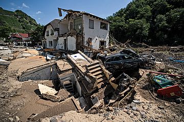 Aufräumarbeiten nach dem Hochwasser: Ein unterspültes Haus mit beschädigtem Auto sind umgeben von Schutt.