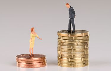 Männliche Figur steht auf einem Stapel 20 Cent Münzen, daneben eine weibliche Figur auf einem deutlich kleinern Stapel 5 Cent Münzen