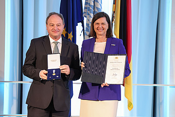 Pfarrer Rainer Maria Schießler mit Verfassungsorden neben Landtagspräsidentin Ilse Aigner, die die dazugehörige Urkunde in der Hand hält