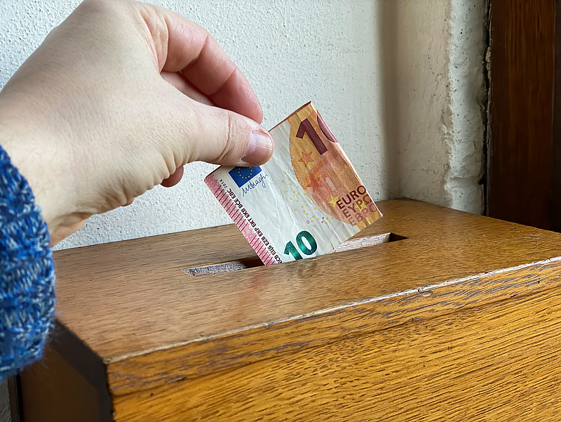 Hand steckt 10-Euro-Schein in einen braunen Kasten