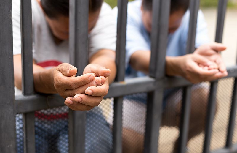 Zwei Menschen knien nieder und strecken die Hände durch ein Gitter.