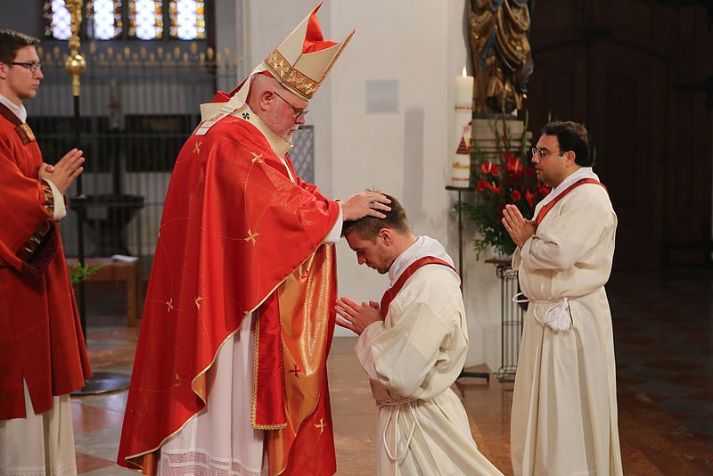 Der Erzbischof von München und Freising, Kardinal Reinhard Marx, legt Gregor Schweizer die Hände auf, rechts von ihm steht sein Mitbruder Jaime-Pasqual Hannig.