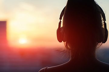 Frau mit Kopfhörern schaut Richtung Sonnenuntergang