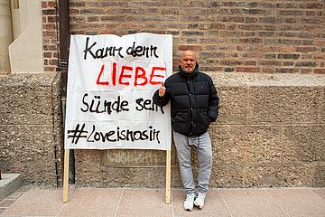 Stefan Alof steht vor dem Liebfrauendom. Neben sich ein Plakat mit der Aufschrift: 